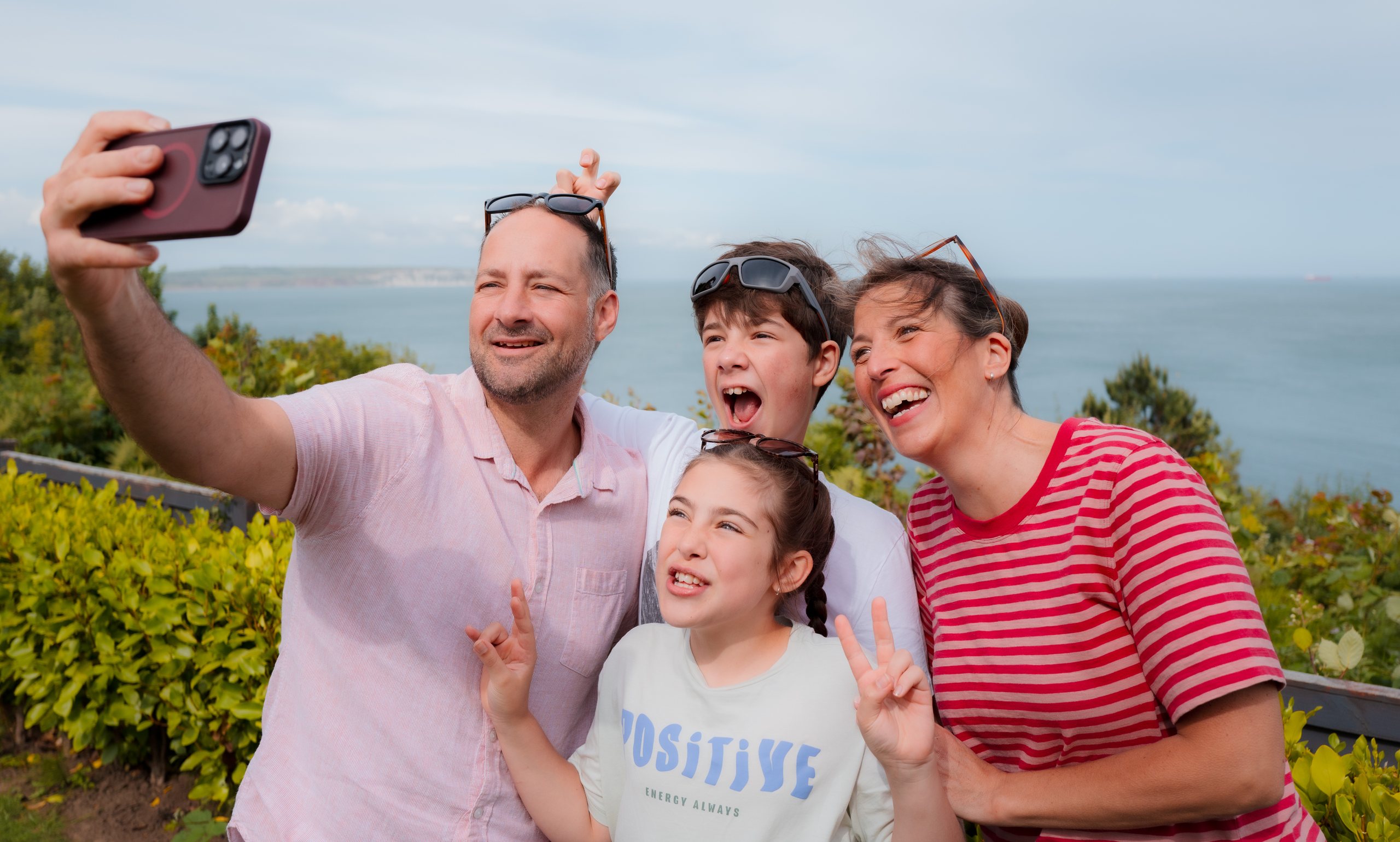 A family taking a selfie on the clifftop at Luccombe Hall with the sea behind them